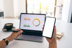 person holding phone in front of a laptop